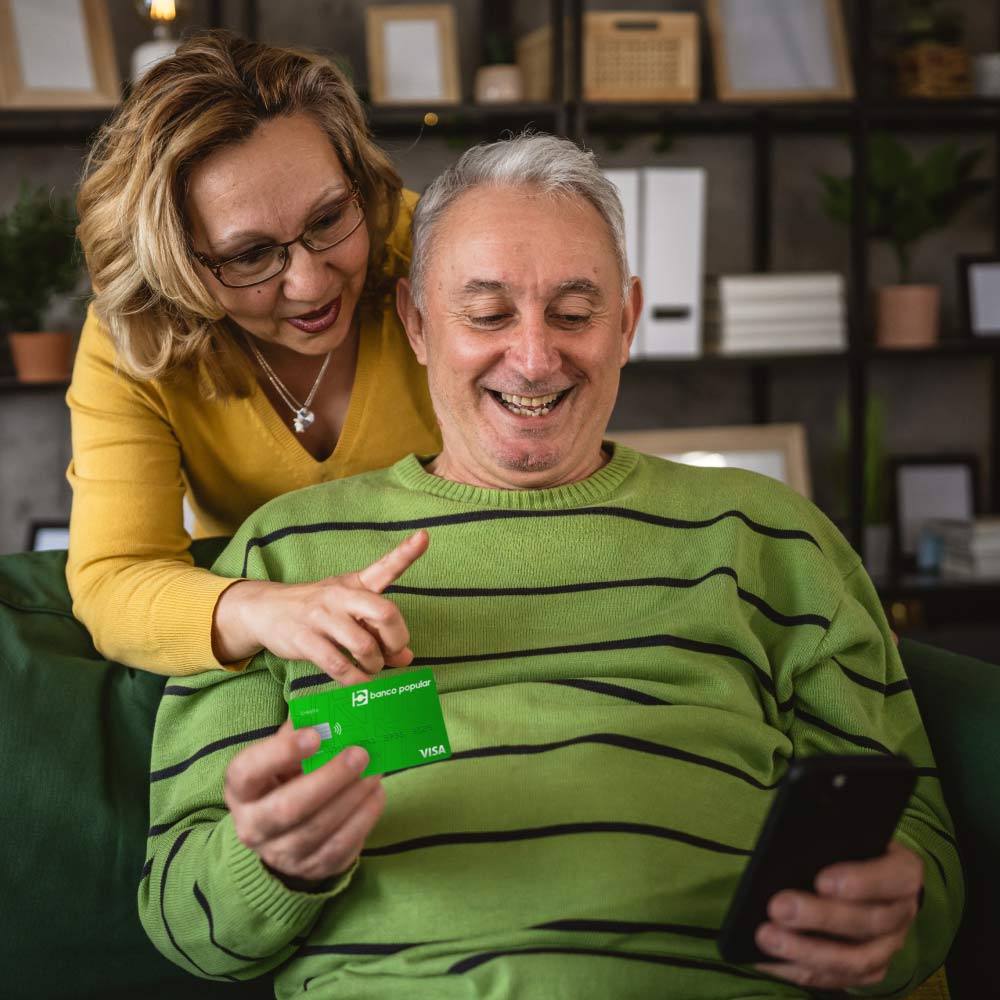 Hombre y mujer viendo el celular con tarjeta del Banco popular en la mano