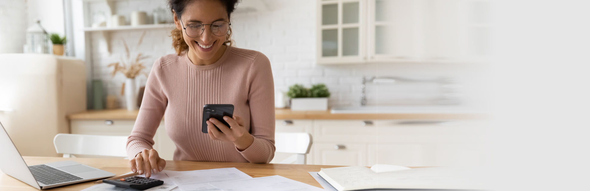 Mujer sonriente en su casa con su telefóno movil en una mano y en la otra con una calculadora