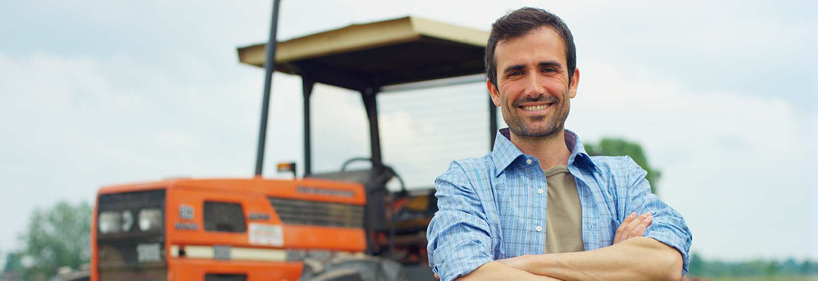 Un granjero joven de camisa azul sonrriendo en frente de su tractor