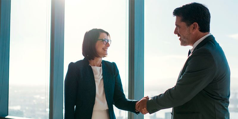 Pareja de empresarios de traje formal estrechando sus manos al haciendo un negocio