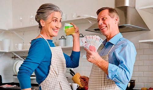 Hombre y mujer en la cocina sonriendo con tarjetas de crédito del Banco Popular y dinero en las manos