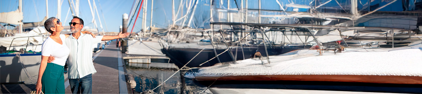 Hombre y mujer mayores de 50 años felices en un puerto rodeados de muchos barcos