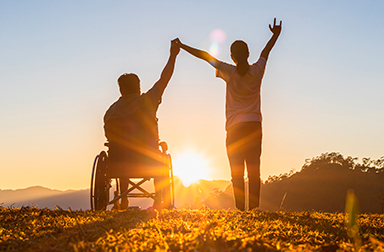dos personas viendo el atardecer a contra luz, una de ellas usa silla de ruedas