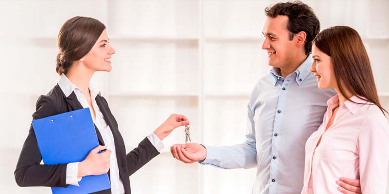 Una pareja recibe de una agente inmobiliario las llaves de su nueva casa