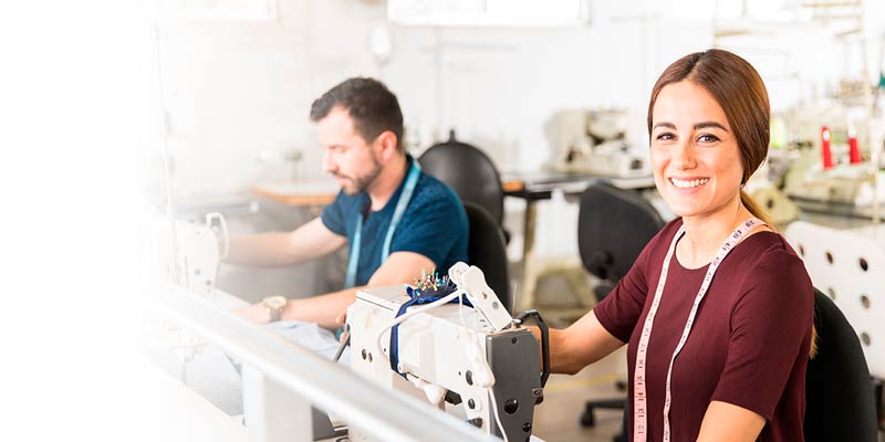 Una joven empresaria con camiseta marron y metro de costura frente a una maquina de coser trabajando en su taller