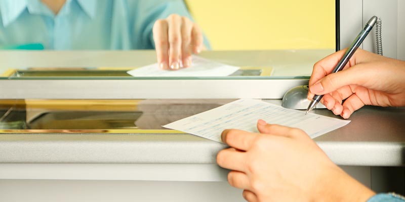 Manos de una mujer escribiendo sobre hoja de papel, esfero 
 de color negro en una ventanilla
 del banco,  realizando una consignación