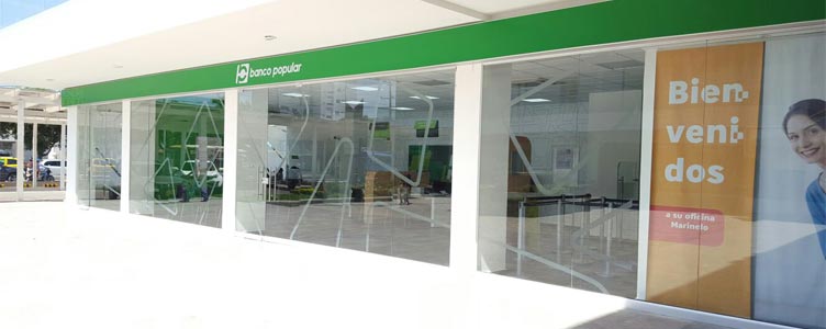Oficina Banco Popular con ventanas de vidrio y logotipo blanco sobre fondo verde