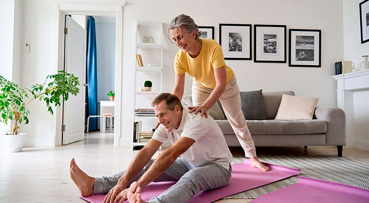 Hombre y mujer mayores de 50 años, haciendo estiramiento sobre tapetes de yoga en su casa