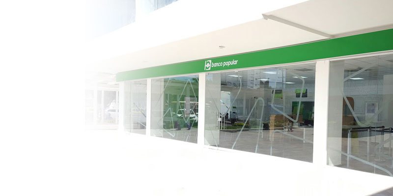 oficinas del Banco Popular con vidrios de cristal y letrero verde con logotipo blanco