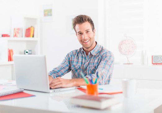 Hombre joven sonriendo mientras trabaja en su computadora portátil