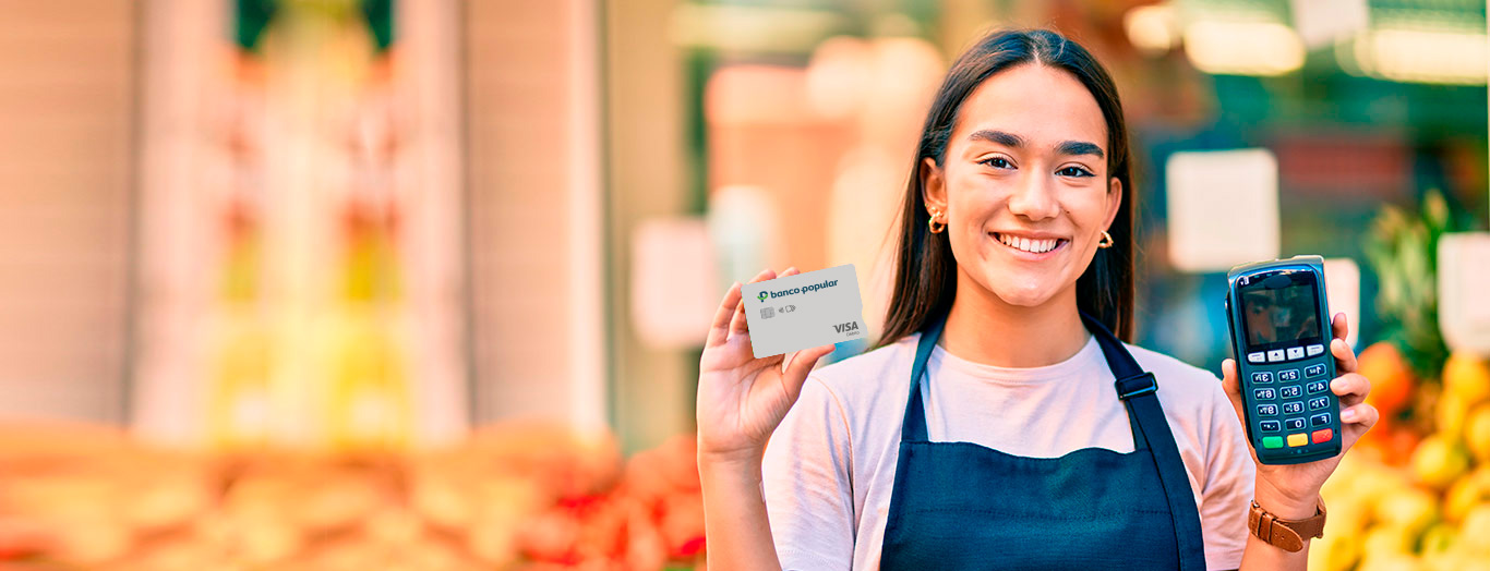 Mujer sonriente con datáfono y tarjeta de creditó del Banco Popular en la mano