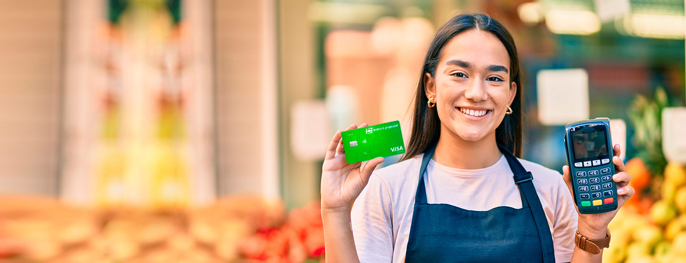 Mujer sonriente con datáfono y tarjeta de creditó del Banco Popular en la mano