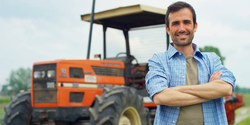 Un granjero joven de camisa azul sonrriendo en frente de su tractor