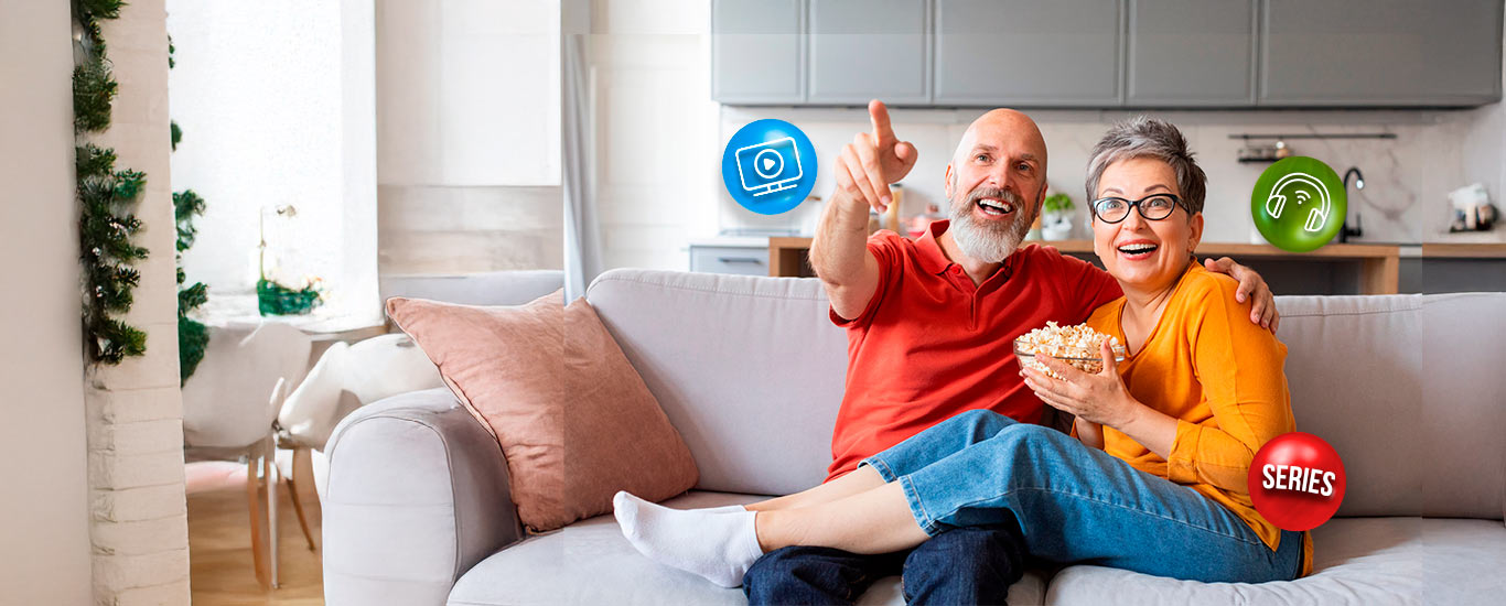 Pareja de mediana edad sonriendo en la sala de su casa al ver los beneficios de su tarjeta de crédito