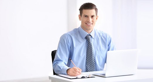 Un ejecutivo con camisa azul y corbata frente al computador consultando las notificaciones del pago en línea de los recaudos