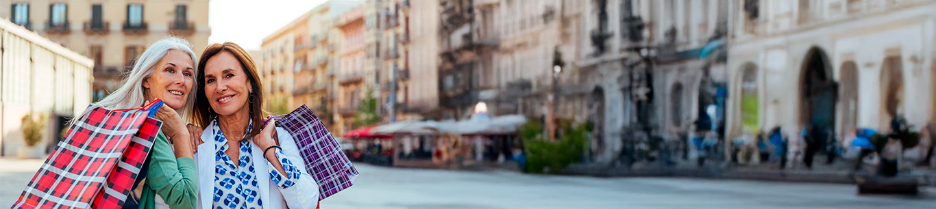 Dos mujeres sonrientes mayores de 50 años con bolsas de compras en una calle de Europa