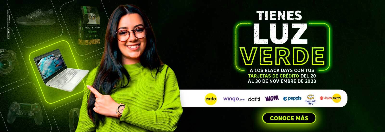 Mujer joven de cabello largo con anteojos y saco verde señalando un computador portátil