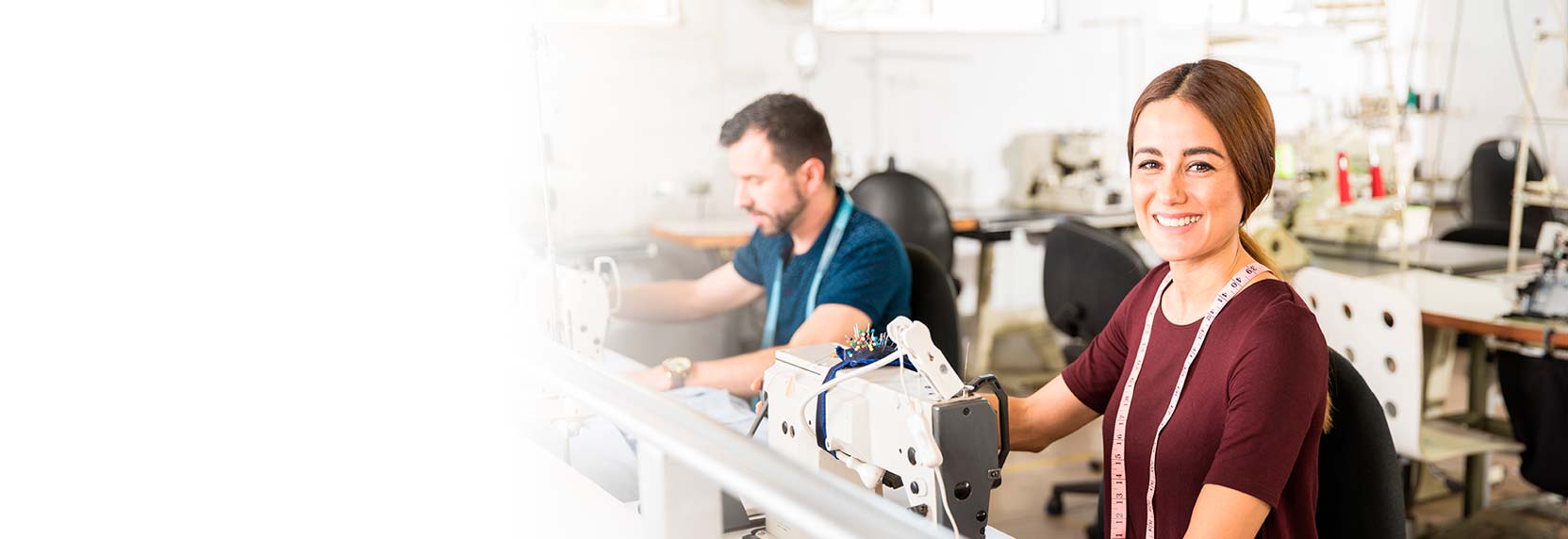 Una joven empresaria con camiseta marron y metro de costura frente a una maquina de coser trabajando en su taller