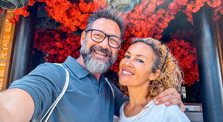 Hombre y mujer mayores de 50 años sonriendo en un bello lugar con muchas flores