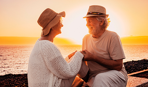 Pareja de personas mayores tomándose de las manos en un atardecer en la playa