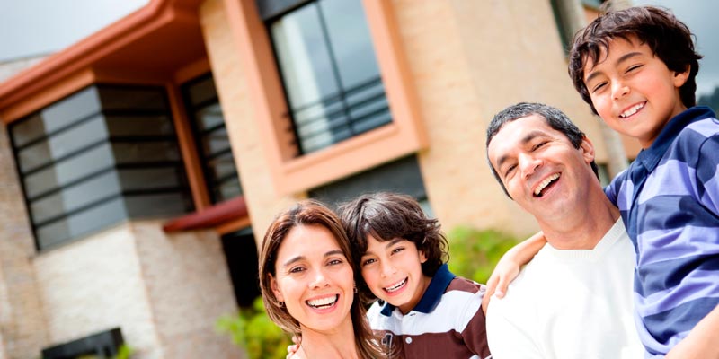 Una pareja con sus dos hijos felices frente de su casa nueva
